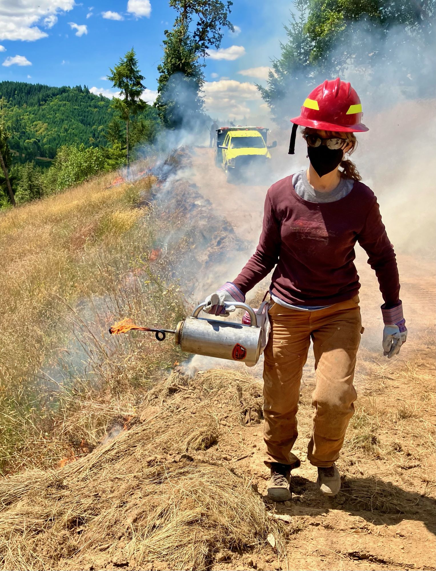 A woman holding a gas canister with a flame, igniting the grass.