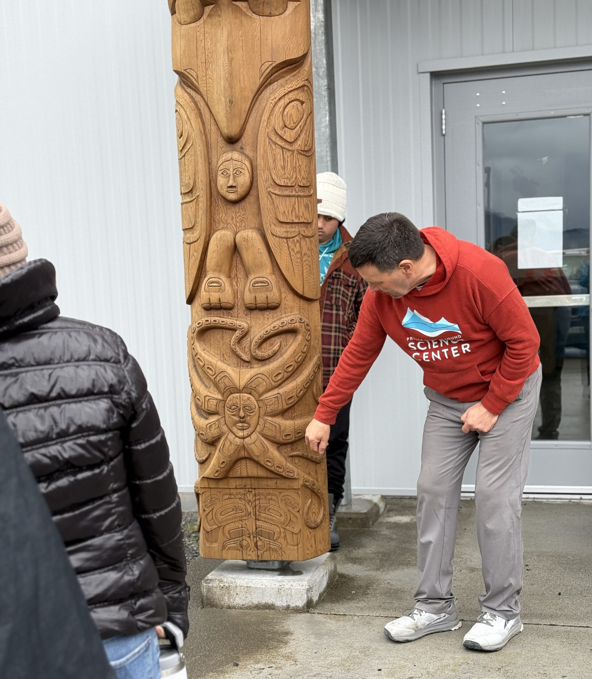 Man examines intricately carved wooden totem pole outdoors