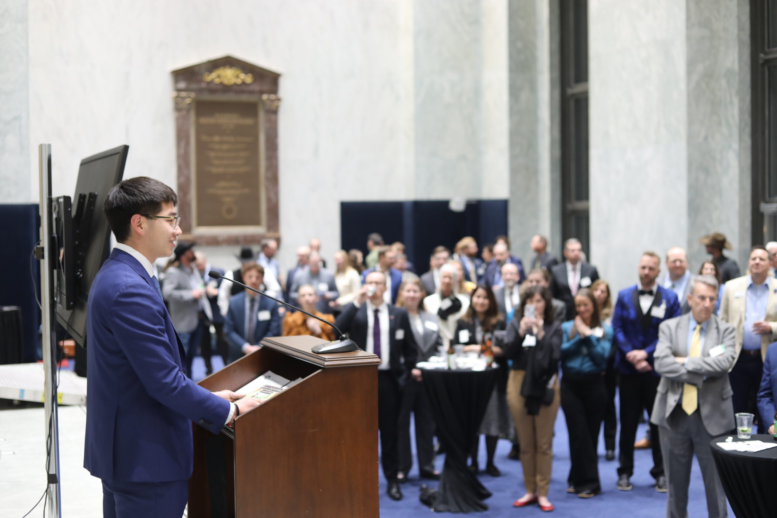 A young man accepts an award and gives a speech in front of a crowded room.