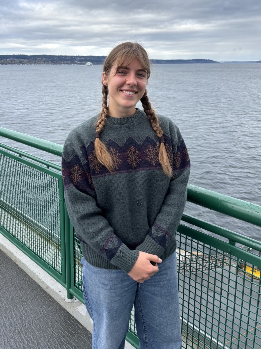 This photo shows a young woman posing for a phot next to a body of water on a cloudy day.