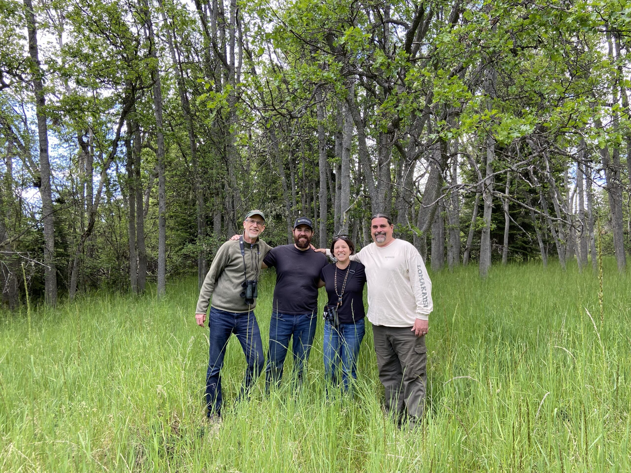 Three men and a woman pose together for a photo in an oak woodland